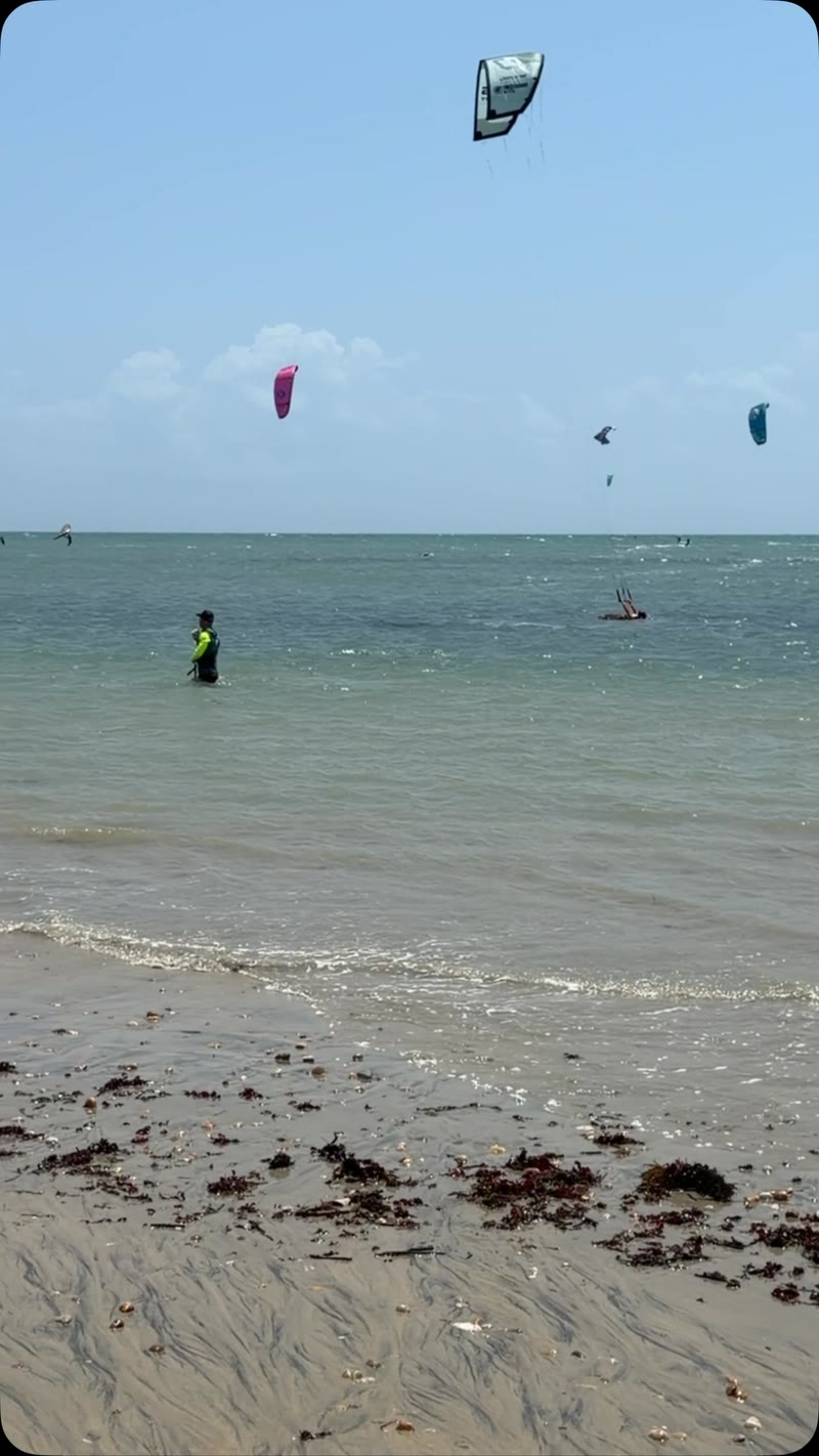 Mar de Cumbuco com vários kites no céu e um instrutor na água