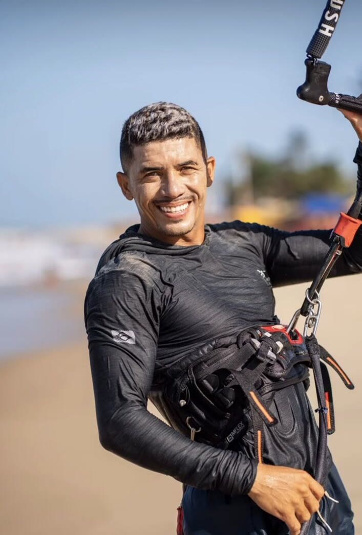 João Carlos sorrindo na praia de Cumbuco, segurando a barra do kite