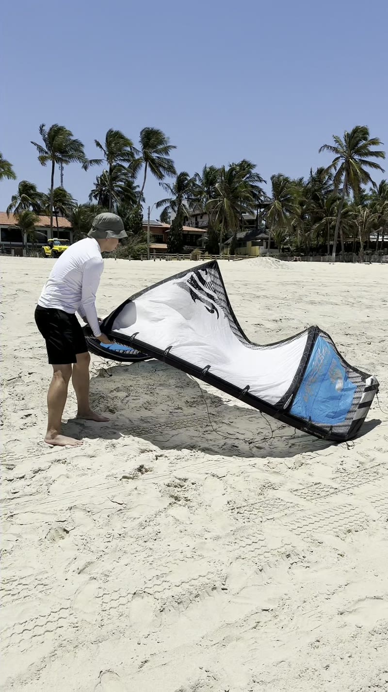 Aluno preparando o kite na areia de Cumbuco, com coqueiros ao fundo